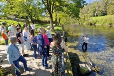 People listening to a talk by Dewi Roberts who is stood in the River Severn at Llanidloes